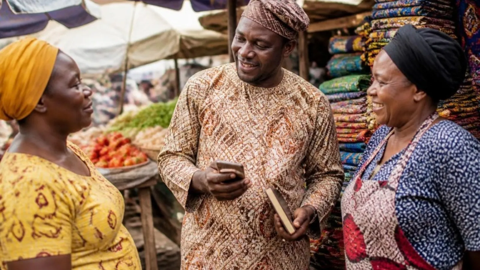 An Ajo collector with his phone, talking with two women traders in a Nigerian market
