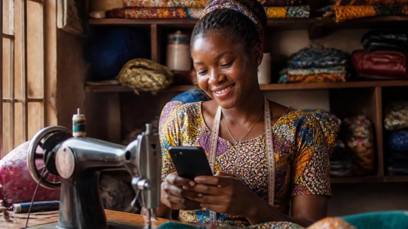 A young tailor smiling at her phone beside her sewing machine