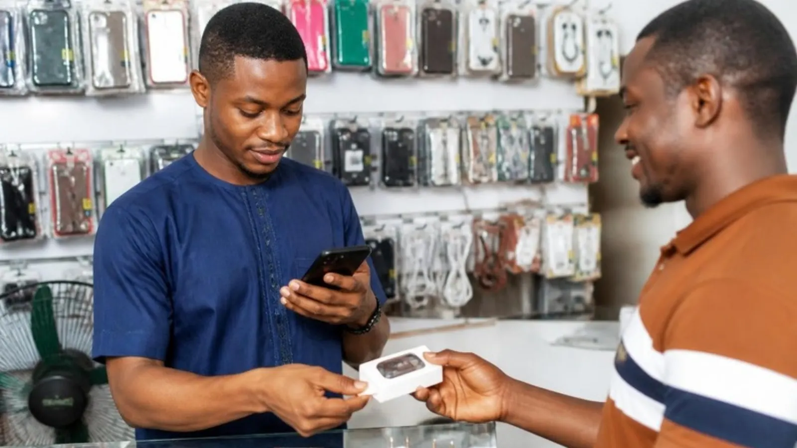 A shop owner records a sale on his phone while a customer pays