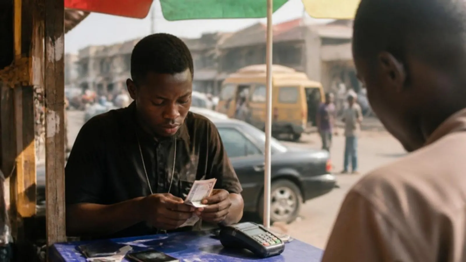 A POS agent counting naira notes at his roadside stand, with a card terminal on the table